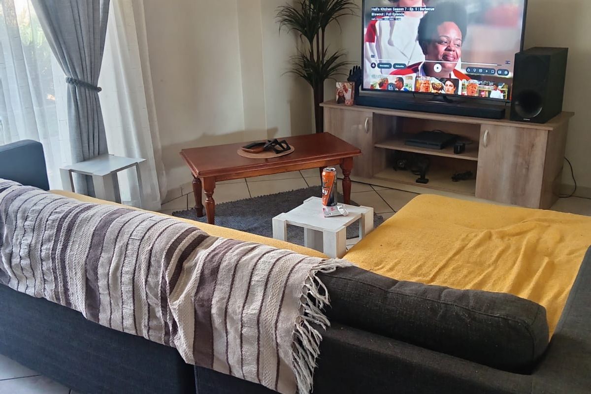 A comfortable living room featuring tiled flooring, large windows with curtains, and a functional layout suitable for relaxation.
