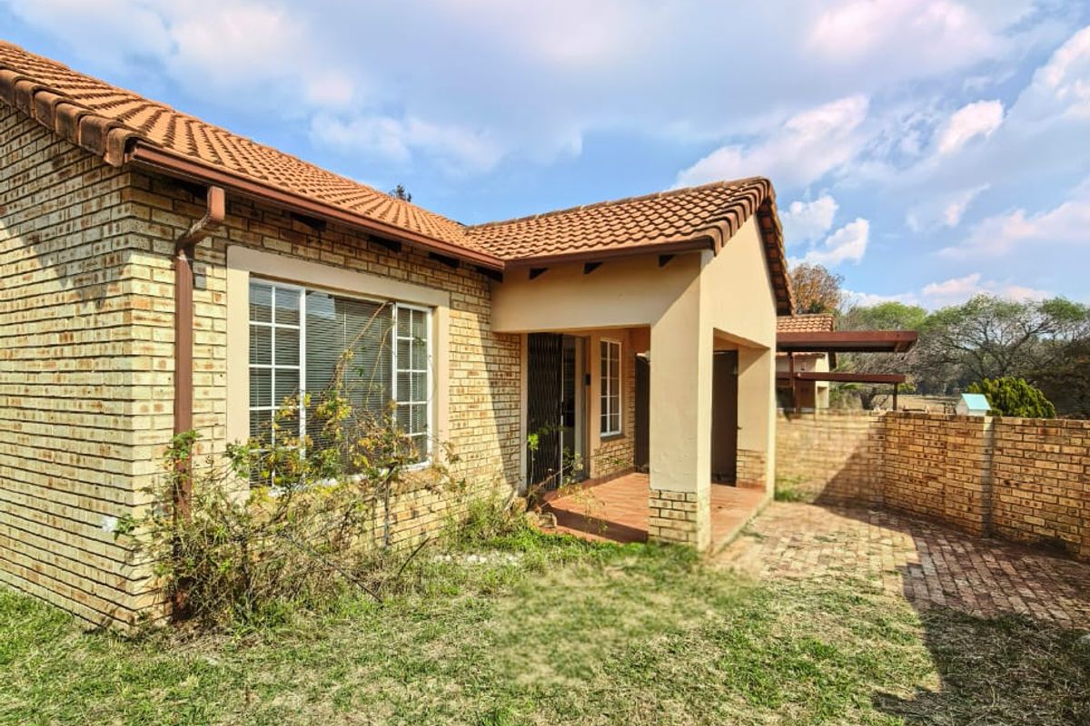 Rear view of the townhouse featuring a brick facade, tiled roof, covered patio area, and a private garden space with brick paving.