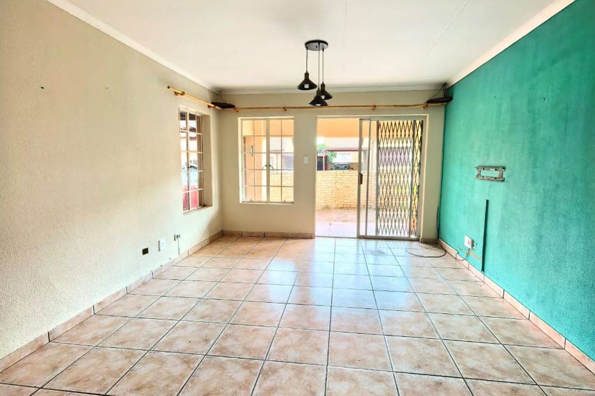 An empty living room featuring ceramic floor tiles, a sliding glass door with security gate, and a distinctive teal accent wall.