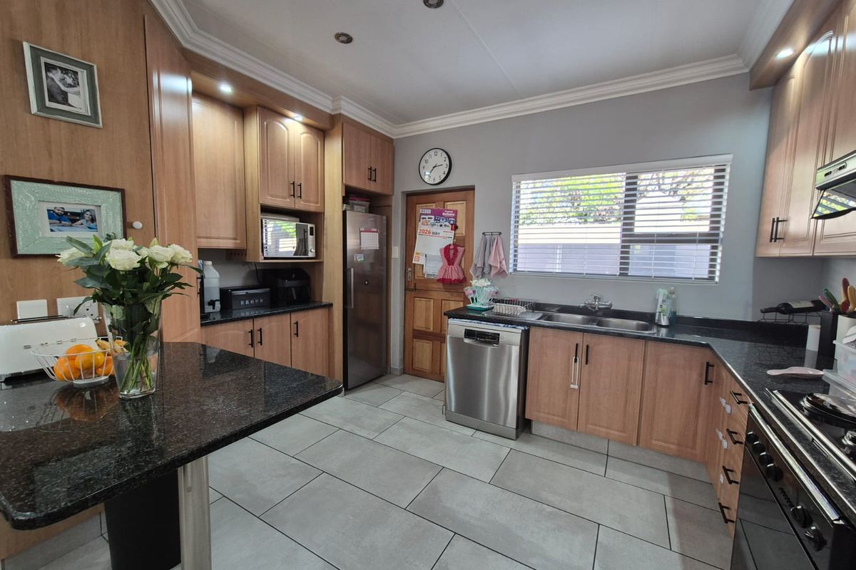 A well-maintained kitchen featuring granite countertops, wooden cabinetry, stainless steel appliances, and tiled flooring with ample natural light.