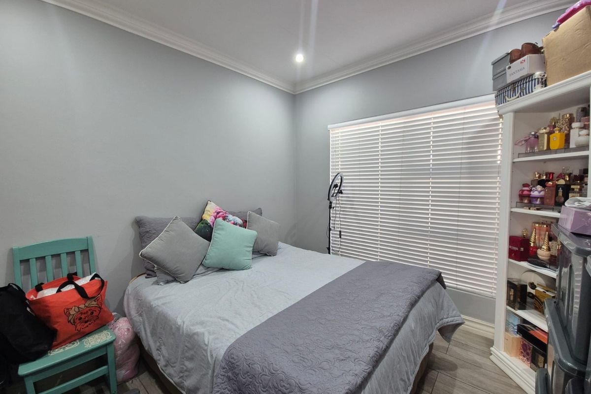 A well-maintained bedroom featuring neutral grey walls, modern laminate flooring, recessed ceiling lighting, and white venetian blinds.