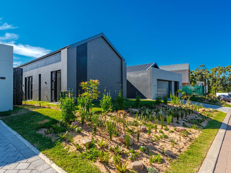 Modern contemporary residential facade featuring dark exterior finishes, paved driveway, and a well-maintained landscaped garden area.
