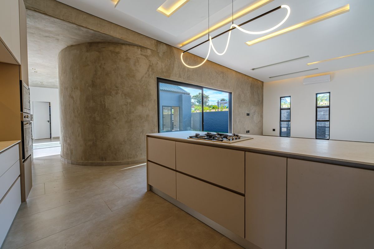 Modern open-plan kitchen featuring a central island with gas hob, built-in oven, sleek cabinetry, and a striking curved concrete feature wall.