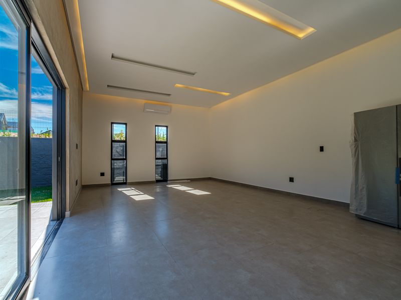 A bright, modern, and empty living area featuring large sliding glass doors, recessed ceiling lighting, and neutral tiled flooring.