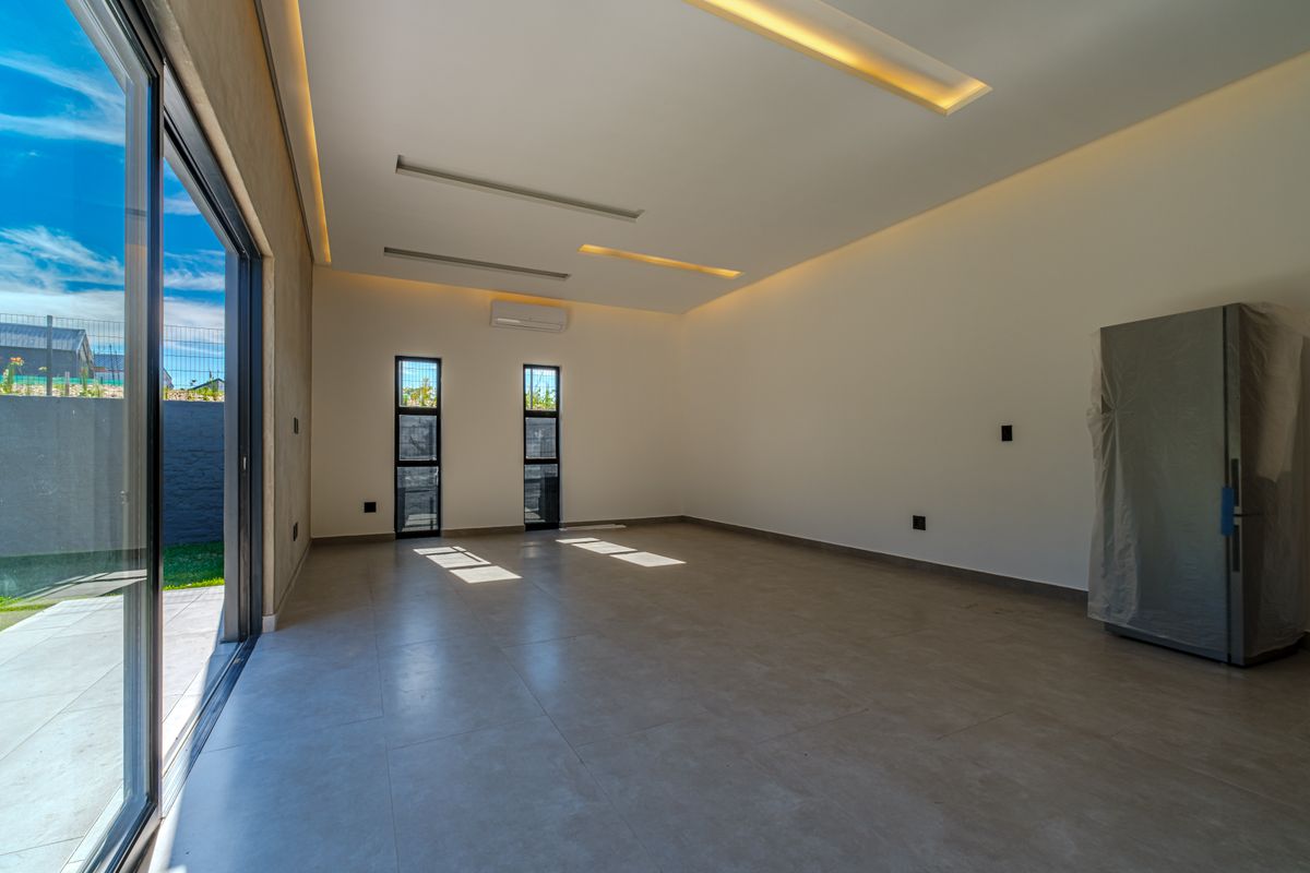 A bright, modern, and empty living area featuring large sliding glass doors, recessed ceiling lighting, and neutral tiled flooring.