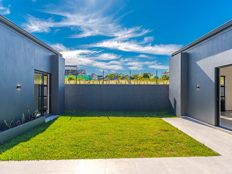A modern, well-maintained rear courtyard featuring a manicured lawn, tiled patio area, and dark-toned exterior walls with integrated lighting.