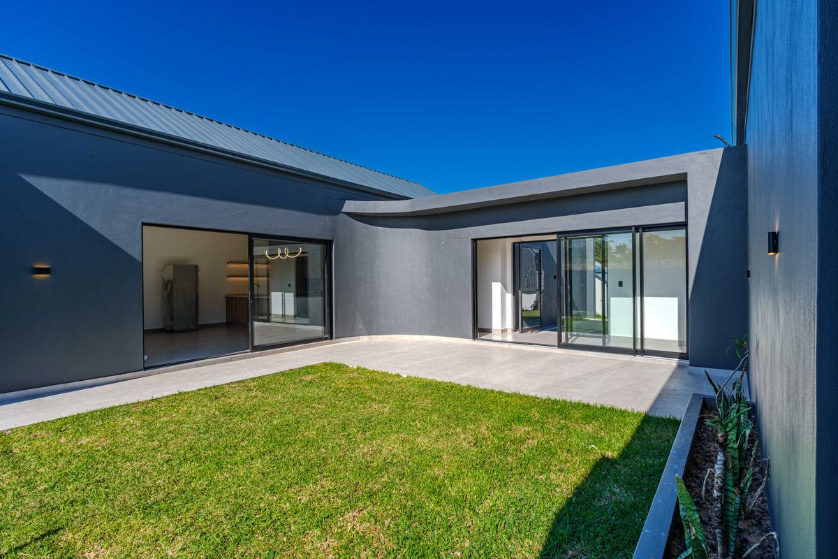 Modern rear courtyard featuring a tiled patio, manicured lawn, built-in planter, and large sliding glass doors providing seamless indoor-outdoor flow.