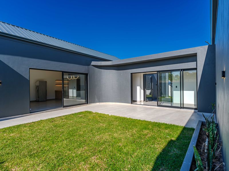 Modern rear courtyard featuring a tiled patio, manicured lawn, built-in planter, and large sliding glass doors providing seamless indoor-outdoor flow.