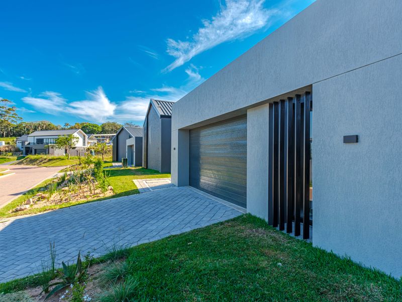 Modern residential exterior featuring a paved driveway, sectional garage door, and contemporary textured facade with vertical slat detailing.