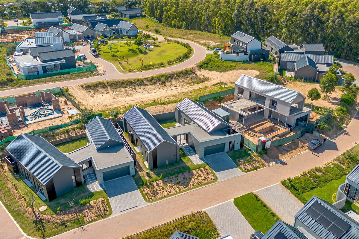 Aerial view of a residential estate development featuring modern homes with metal roofs, paved driveways, and ongoing construction work.