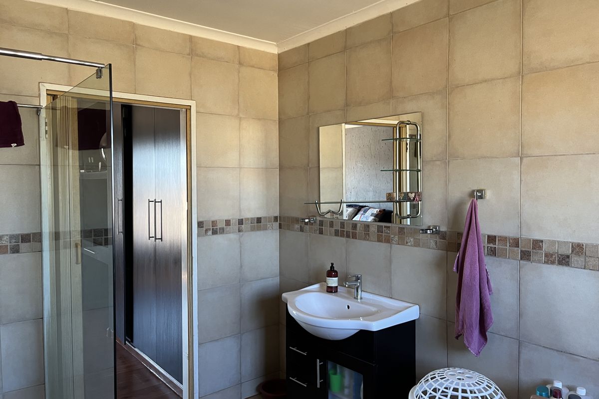 A functional bathroom featuring a glass-enclosed shower, a wall-mounted vanity with basin, and neutral wall tiling with a decorative mosaic border.