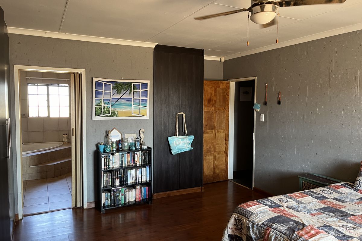Spacious bedroom featuring dark wood-look flooring, a ceiling fan, and direct access to an en-suite bathroom with a corner bathtub.