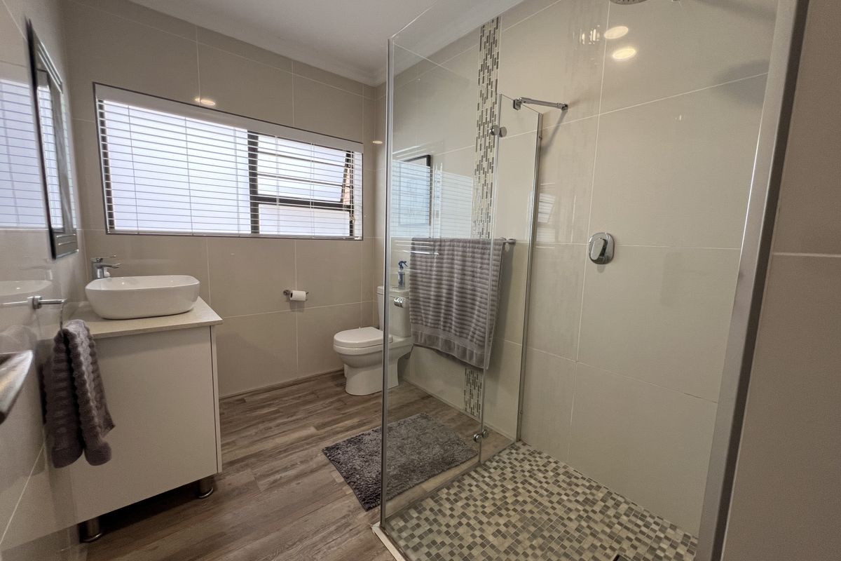 Modern bathroom featuring a glass-enclosed walk-in shower with mosaic tile flooring, a contemporary vanity with vessel sink, and neutral wall tiling.