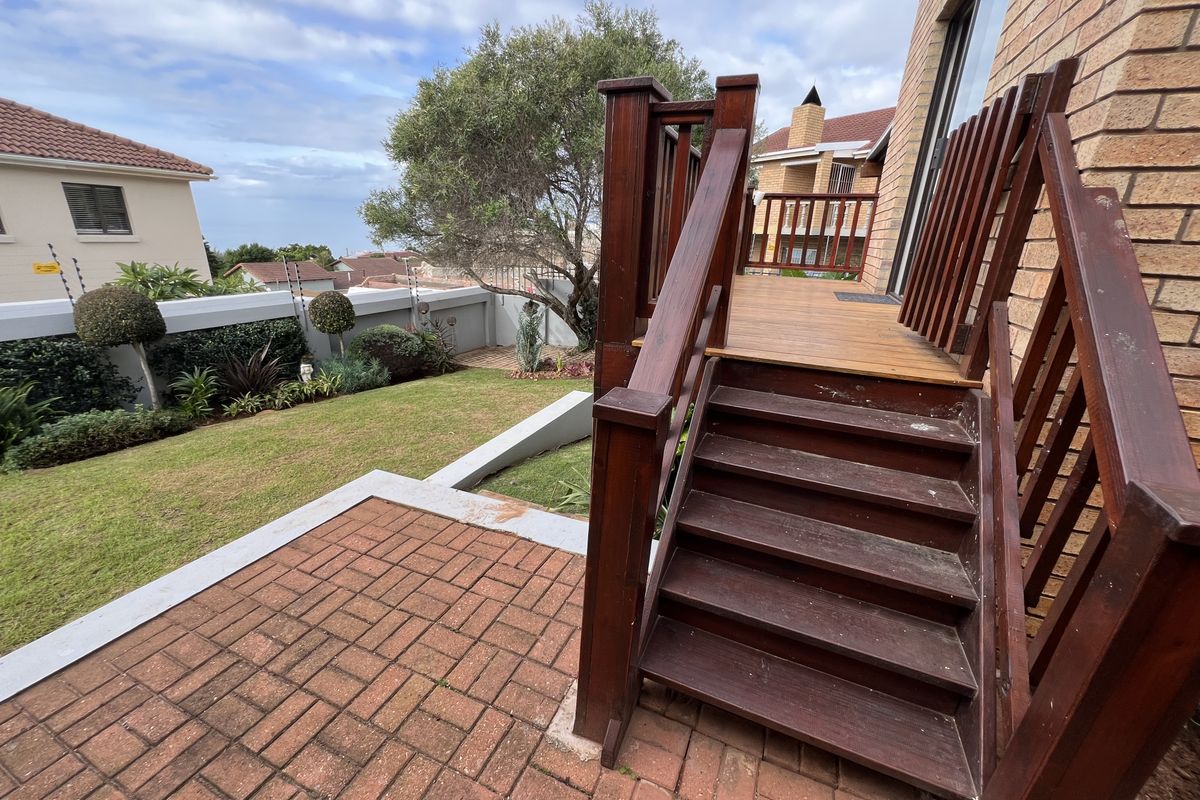 A rear exterior view featuring a raised timber deck with stairs leading down to a paved patio area and a landscaped garden.
