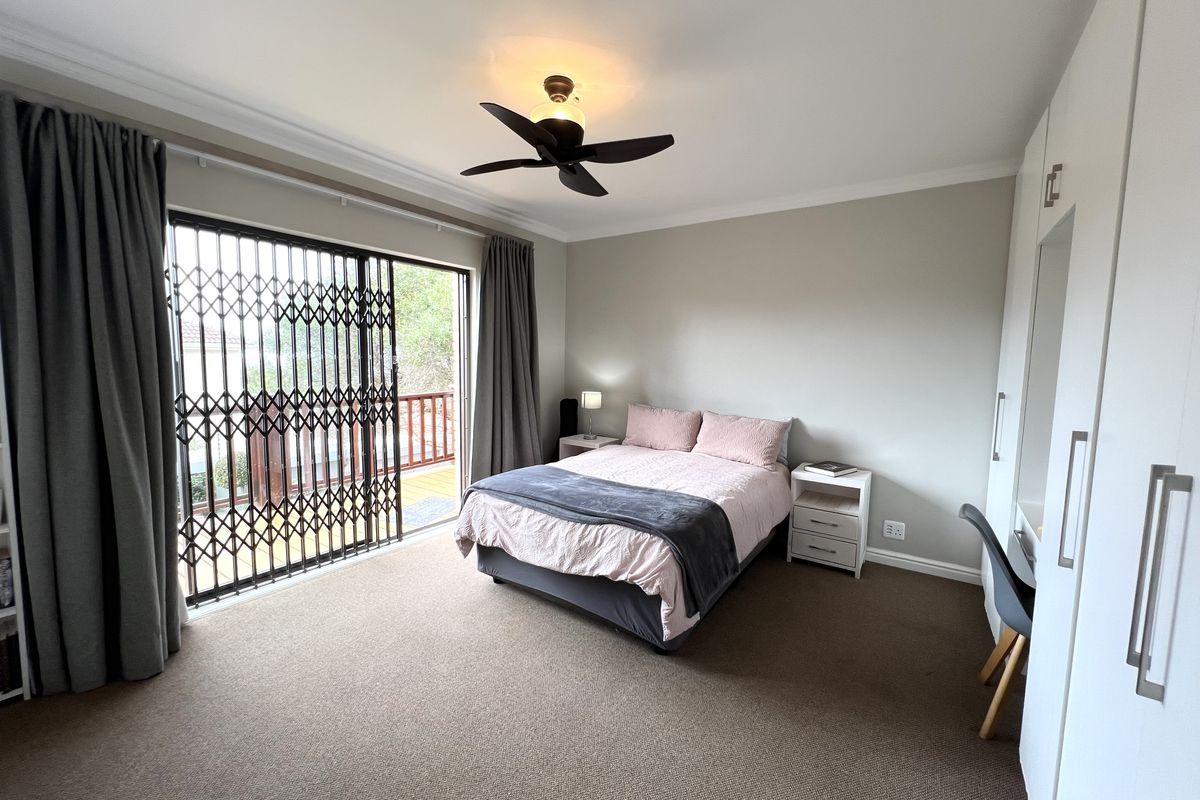 A well-maintained bedroom featuring neutral carpeting, built-in wardrobes, a ceiling fan, and sliding glass doors with security gates leading to an outdoor balcony.