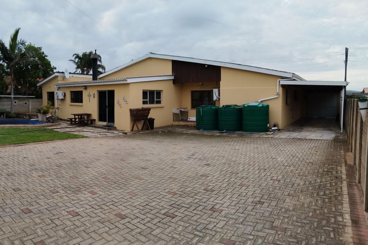 Rear view of the property featuring a paved driveway, carport, water storage tanks, and a small garden area.