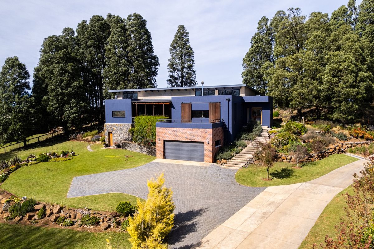 Aerial view of a modern multi-level residence featuring a brick and blue facade, integrated garage, stone retaining walls, and landscaped garden surroundings.