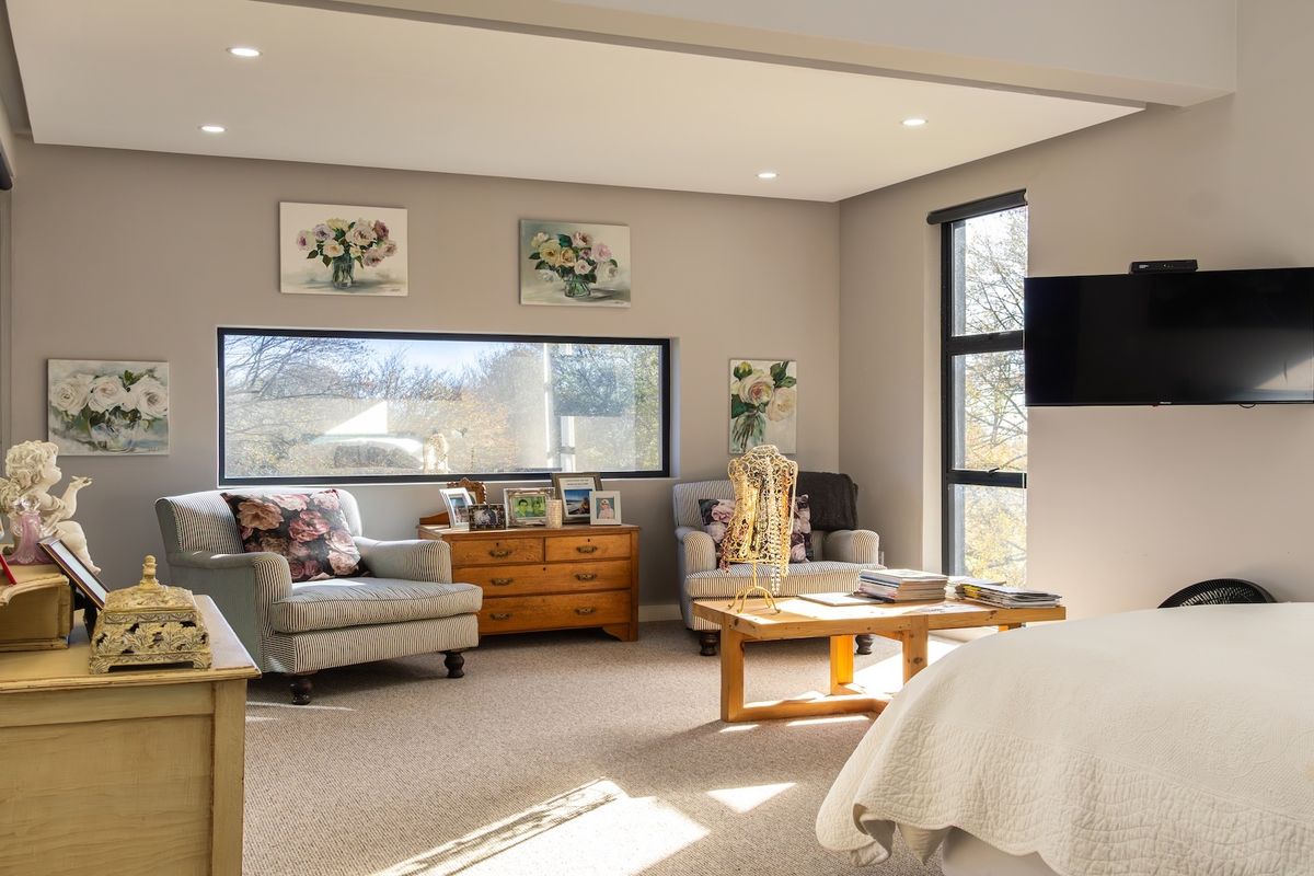 A spacious, well-lit bedroom featuring large windows, recessed ceiling lighting, and neutral carpeting, creating a comfortable and inviting atmosphere.