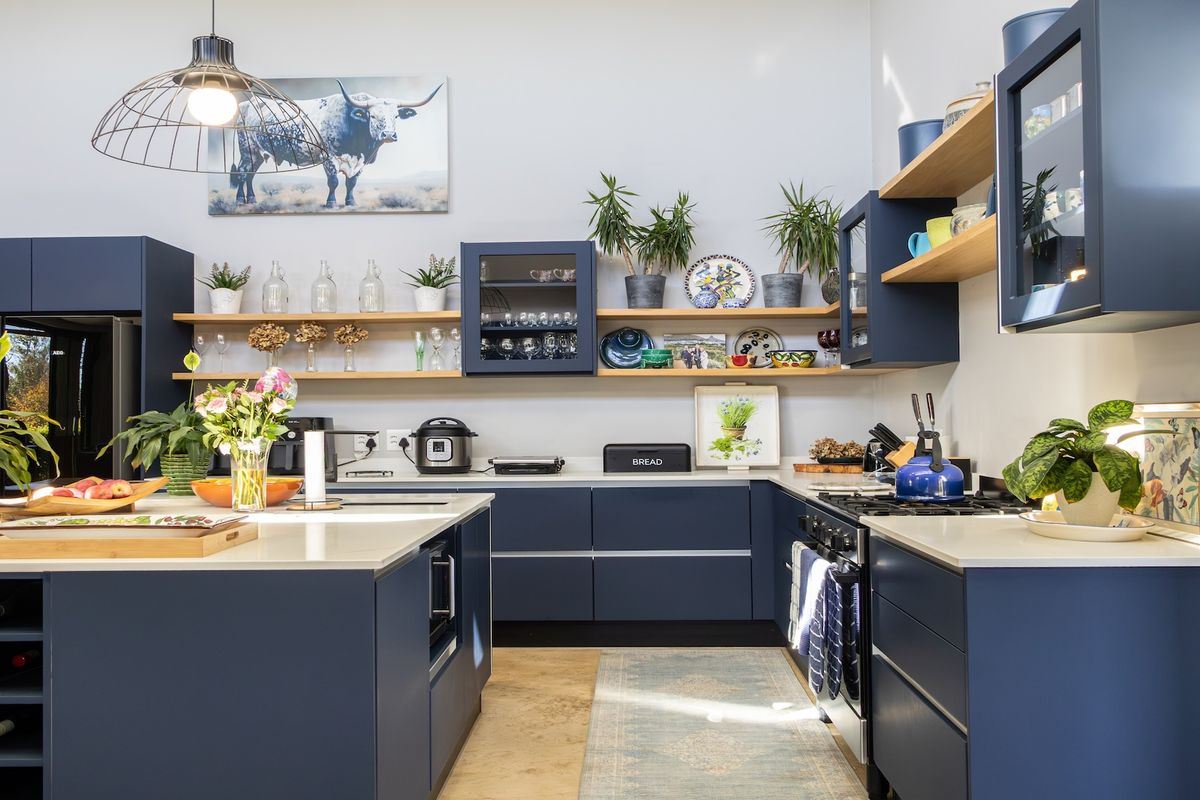 Modern kitchen featuring navy blue cabinetry, stone countertops, open timber shelving, and a central island with integrated wine storage.