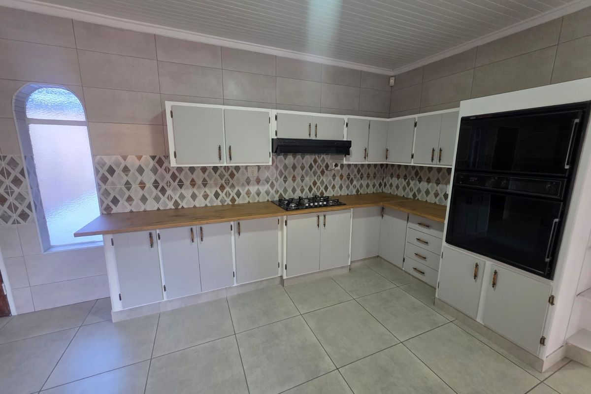 A functional kitchen featuring light-toned cabinetry, wood-look countertops, a built-in oven, gas hob, extractor fan, and decorative tiled backsplash.