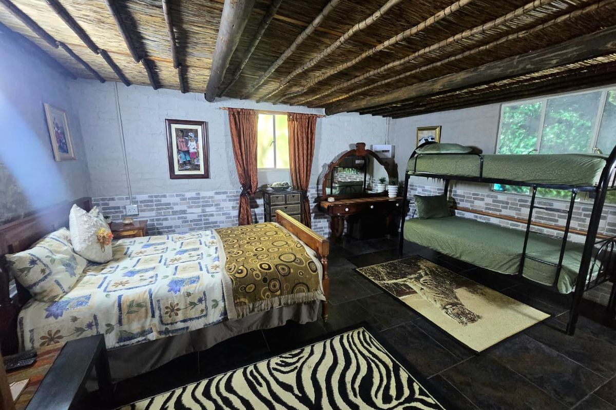 Spacious bedroom featuring a rustic exposed timber beam and thatched ceiling, tiled flooring, and decorative brick-style wall finishes.