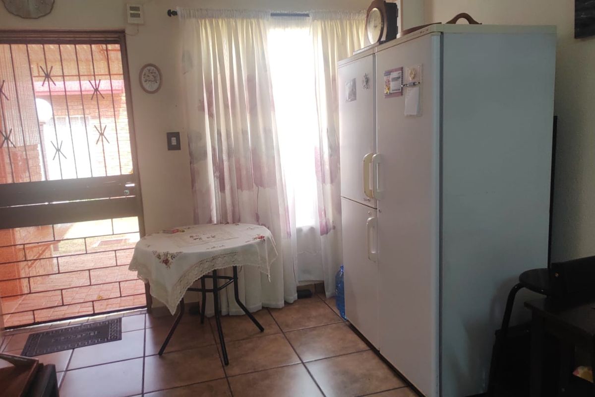 A functional living area featuring tiled flooring, a security gate at the entrance, and natural light through a window with curtains.