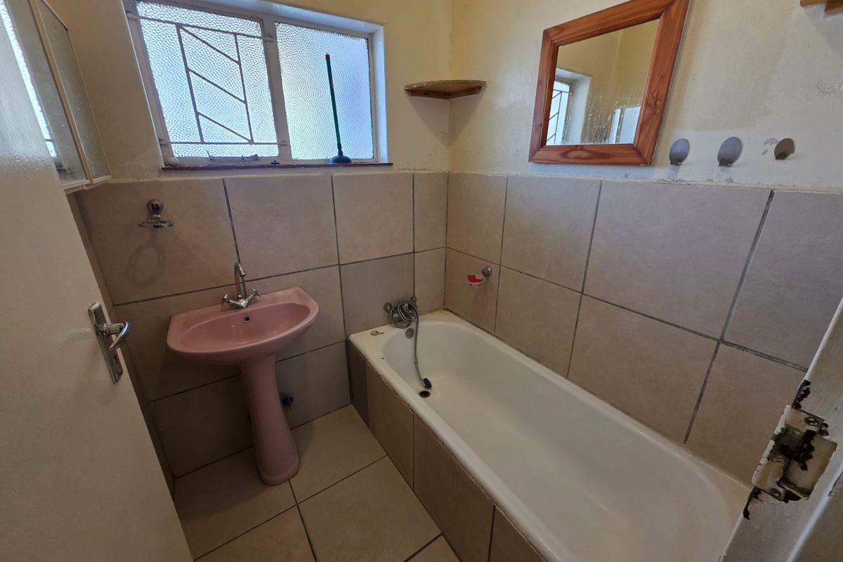 A compact bathroom featuring a pedestal sink, bathtub with shower mixer, and tiled walls, requiring cosmetic updates to modernize the space.