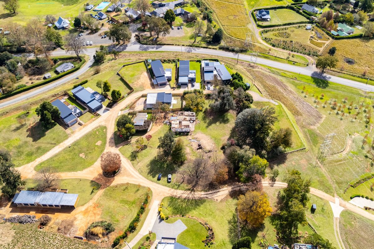 Aerial view of a residential land plot featuring established trees, surrounding road infrastructure, and neighboring properties in a rural estate setting.