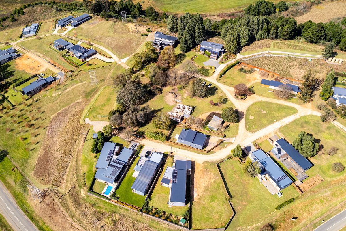 Aerial view of a residential estate featuring multiple modern homes with metal roofs, landscaped grounds, and established trees in a rural setting.