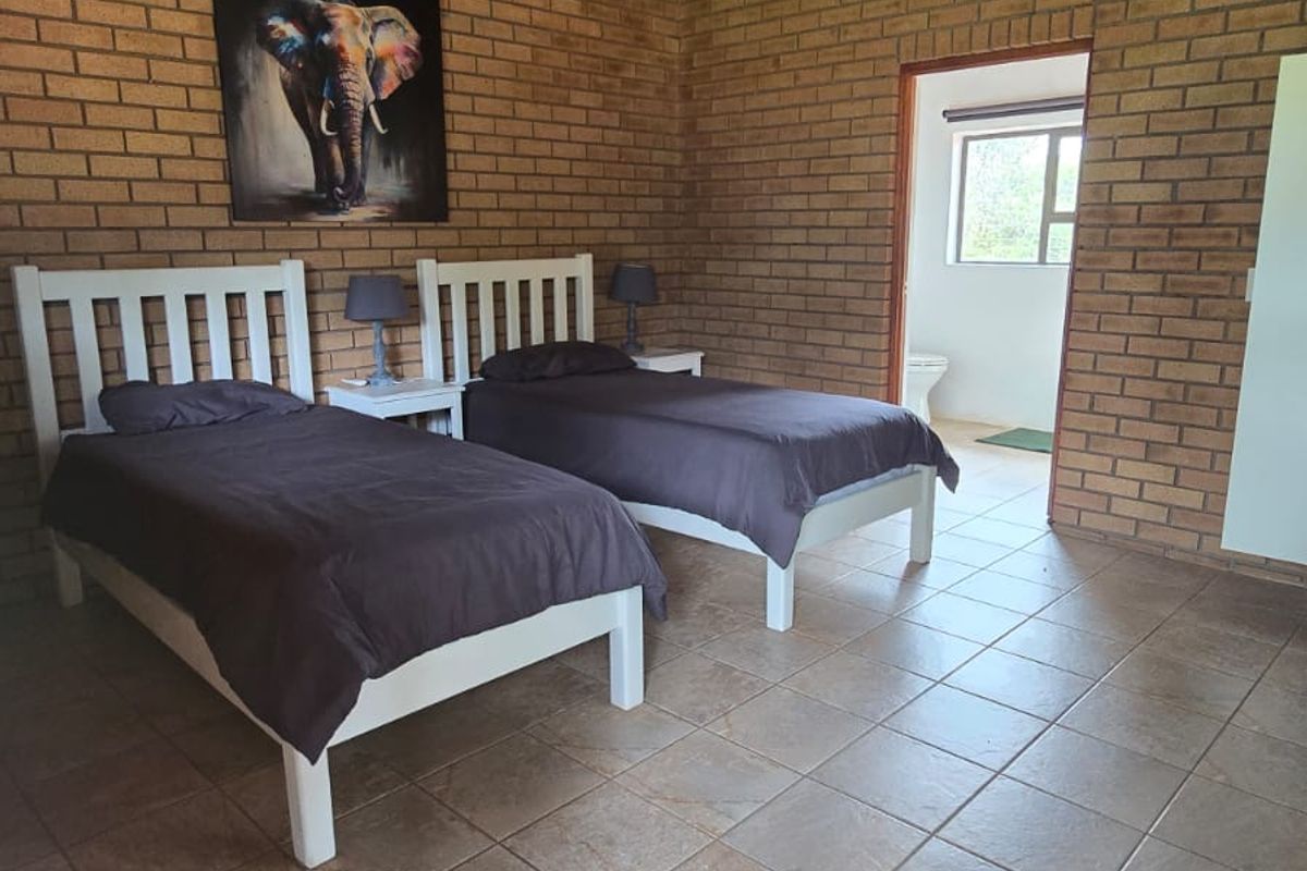 Spacious bedroom featuring exposed brick walls, a high thatched ceiling with a ceiling fan, and tiled flooring, with an adjoining en-suite bathroom.