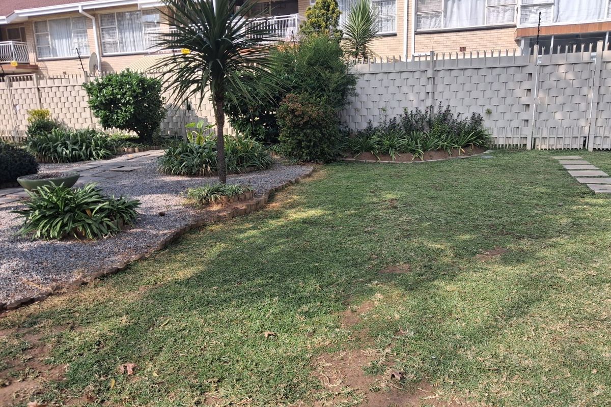 A private rear garden featuring a lawn area, gravel landscaping, established shrubs, and a perimeter boundary wall.