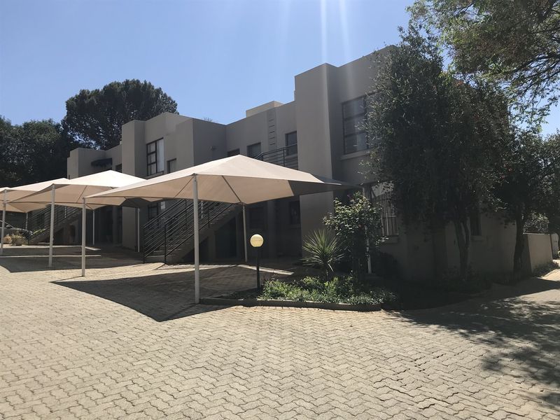 Exterior view of a townhouse complex featuring paved driveway, covered parking bays, and established landscaping.