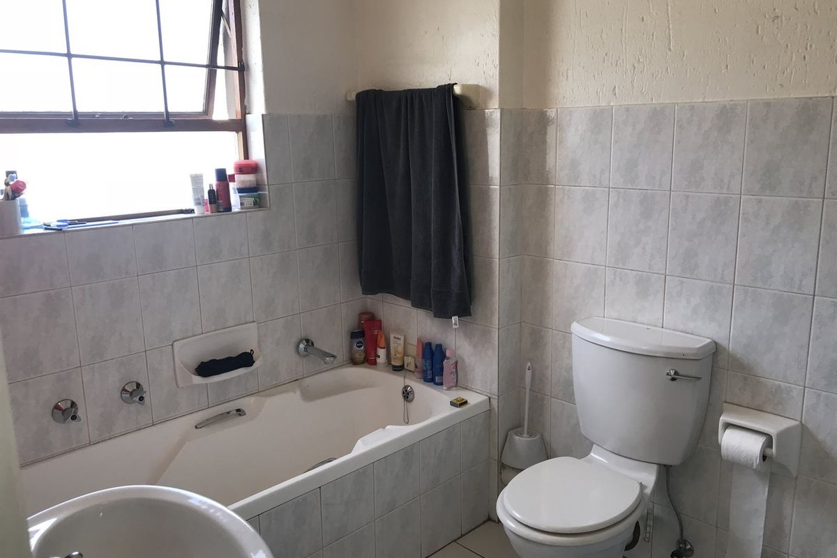 A functional bathroom featuring a built-in bathtub, a standard toilet, and tiled wall finishes with a window for natural light.