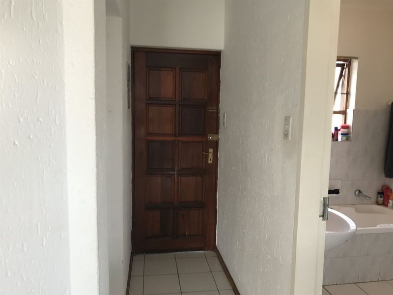A functional hallway featuring a solid timber entrance door and tiled flooring, providing access to the adjacent bathroom area.