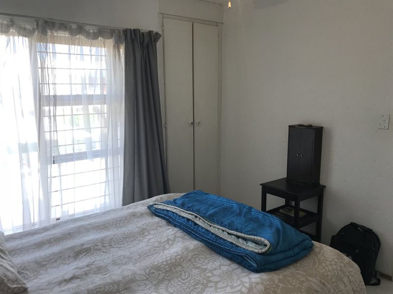 A bedroom featuring a built-in cupboard and a large window with security bars, providing natural light.