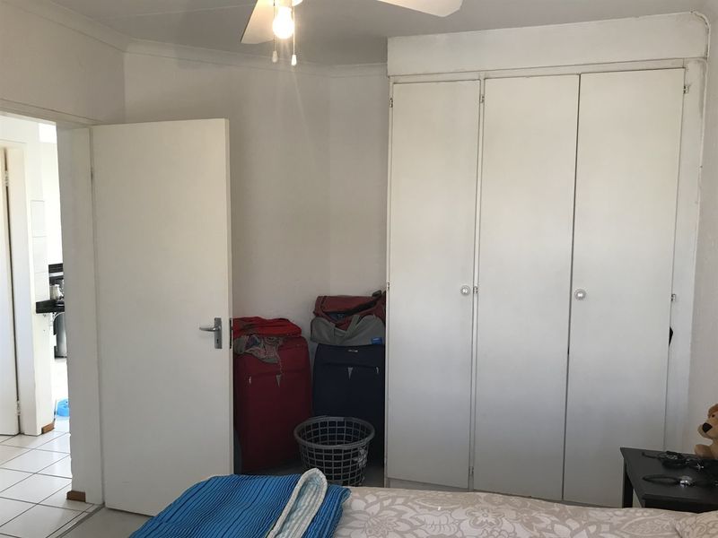 A bedroom featuring built-in cupboards and a ceiling fan, with an adjacent view into a tiled hallway.