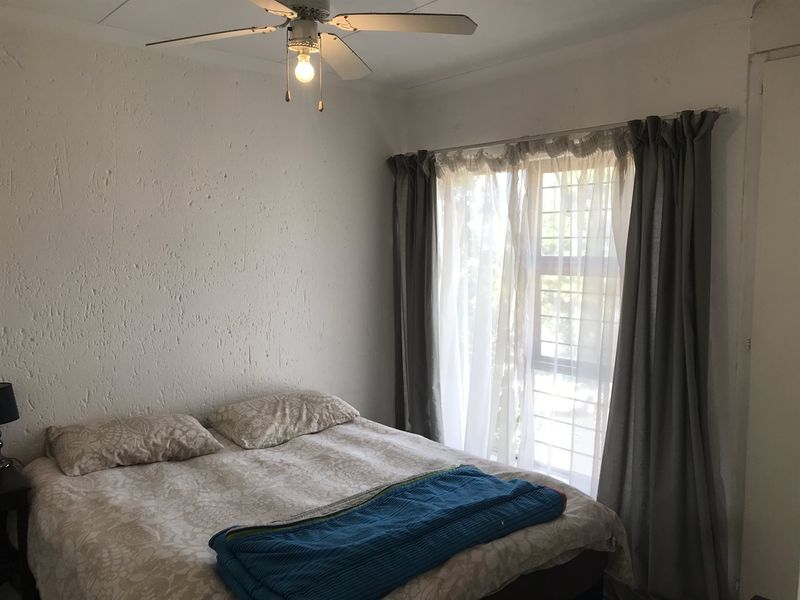 A bedroom featuring a ceiling fan and a window with security bars, providing natural light and ventilation.