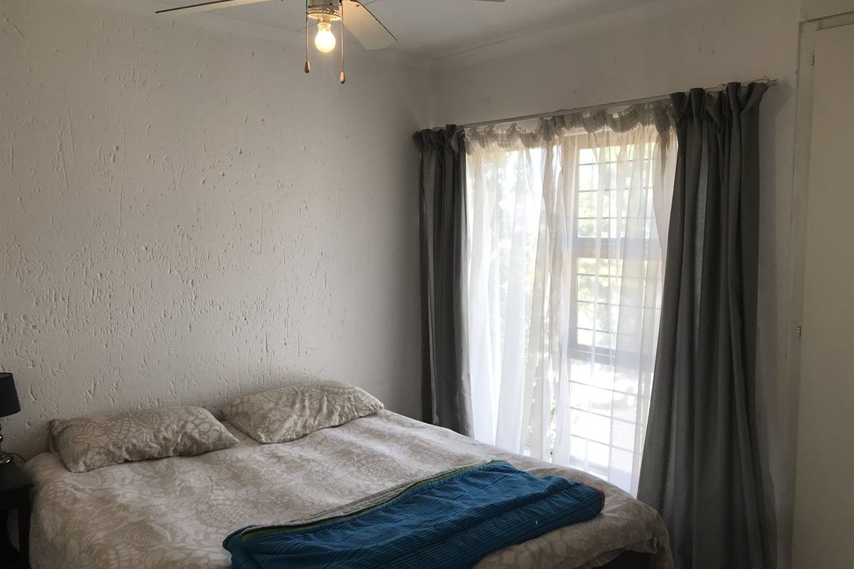 A bedroom featuring a ceiling fan and a window with security bars, providing natural light and ventilation.