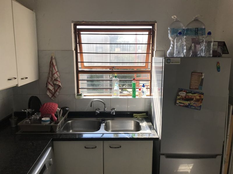 A compact kitchen area featuring a double stainless steel sink, dark granite countertops, and white cabinetry with a window overlooking the exterior.