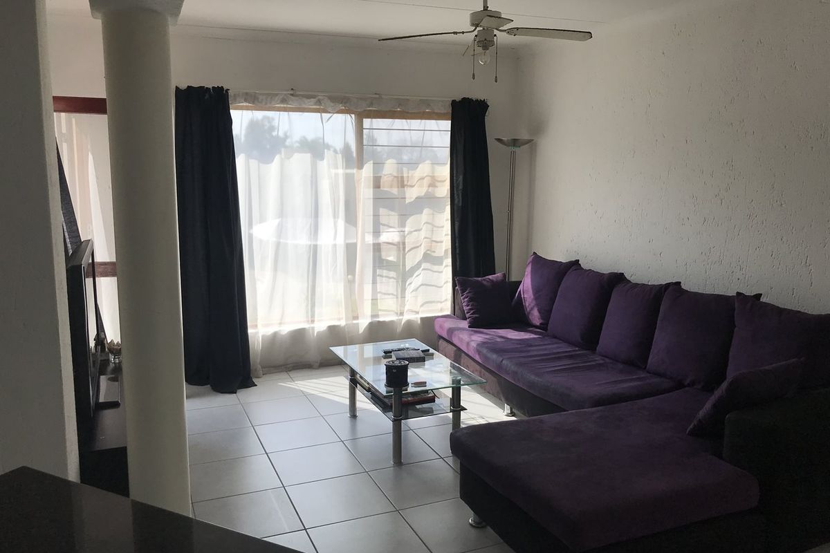 A living room featuring tiled flooring, a ceiling fan, and large windows that provide natural light.