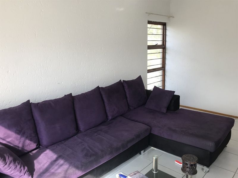 A living room featuring tiled flooring and a window with a metal frame, providing a functional and neutral space for relaxation.