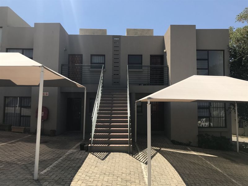 Exterior view of a townhouse complex featuring a central staircase, paved parking area, and shade cloth carports.