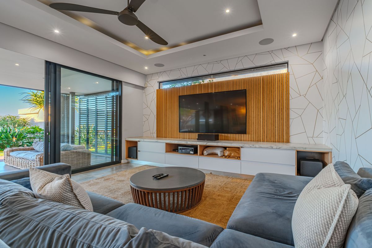 Modern living room featuring a custom timber slat feature wall, built-in cabinetry, recessed ceiling with fan, and large sliding doors opening to a patio.