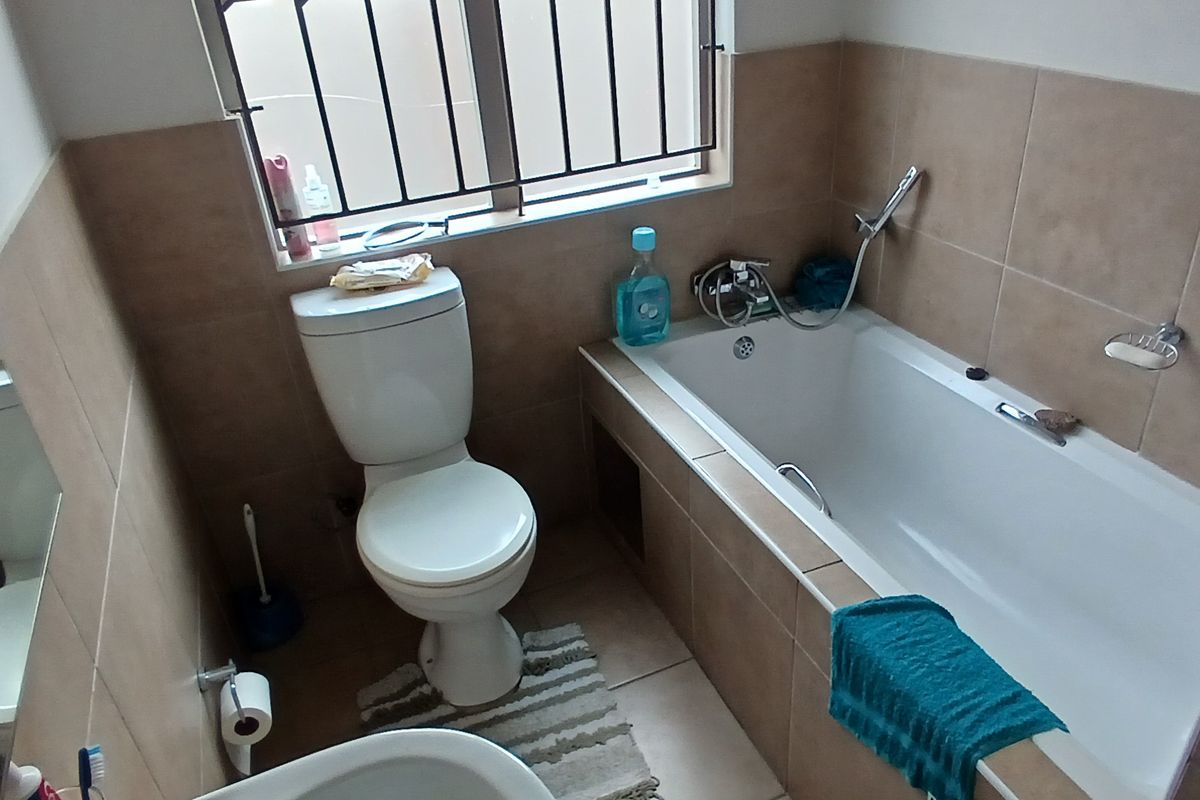 A functional bathroom featuring a built-in bathtub, toilet, and tiled walls with security bars on the windows.