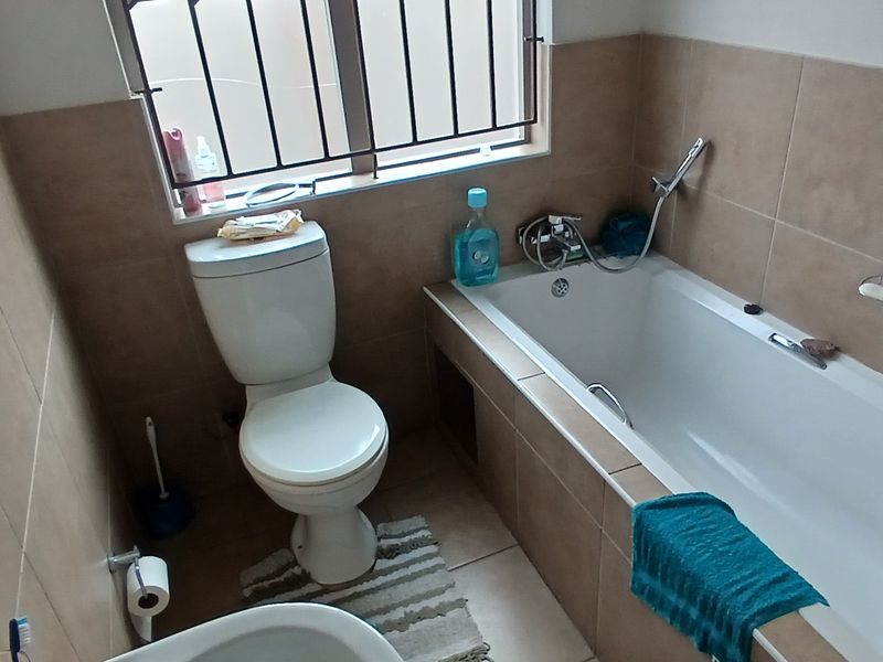 A functional bathroom featuring a built-in bathtub, toilet, and tiled walls with security bars on the windows.