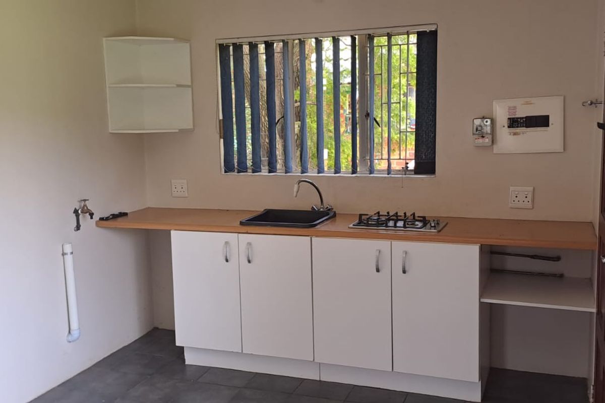 A functional kitchenette featuring white cabinetry, a built-in gas hob, a sink, and a wooden countertop, suitable for a small studio or utility space.