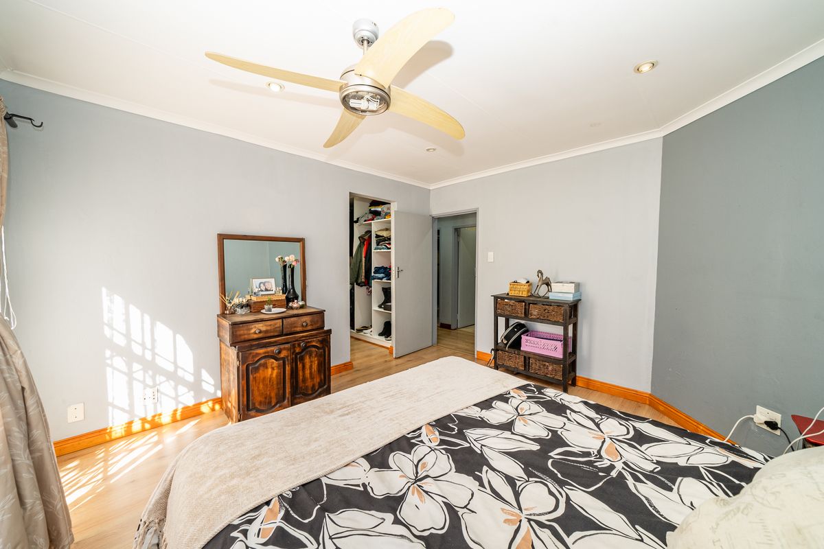 A well-lit bedroom featuring a ceiling fan, laminate flooring, and a built-in closet with shelving.