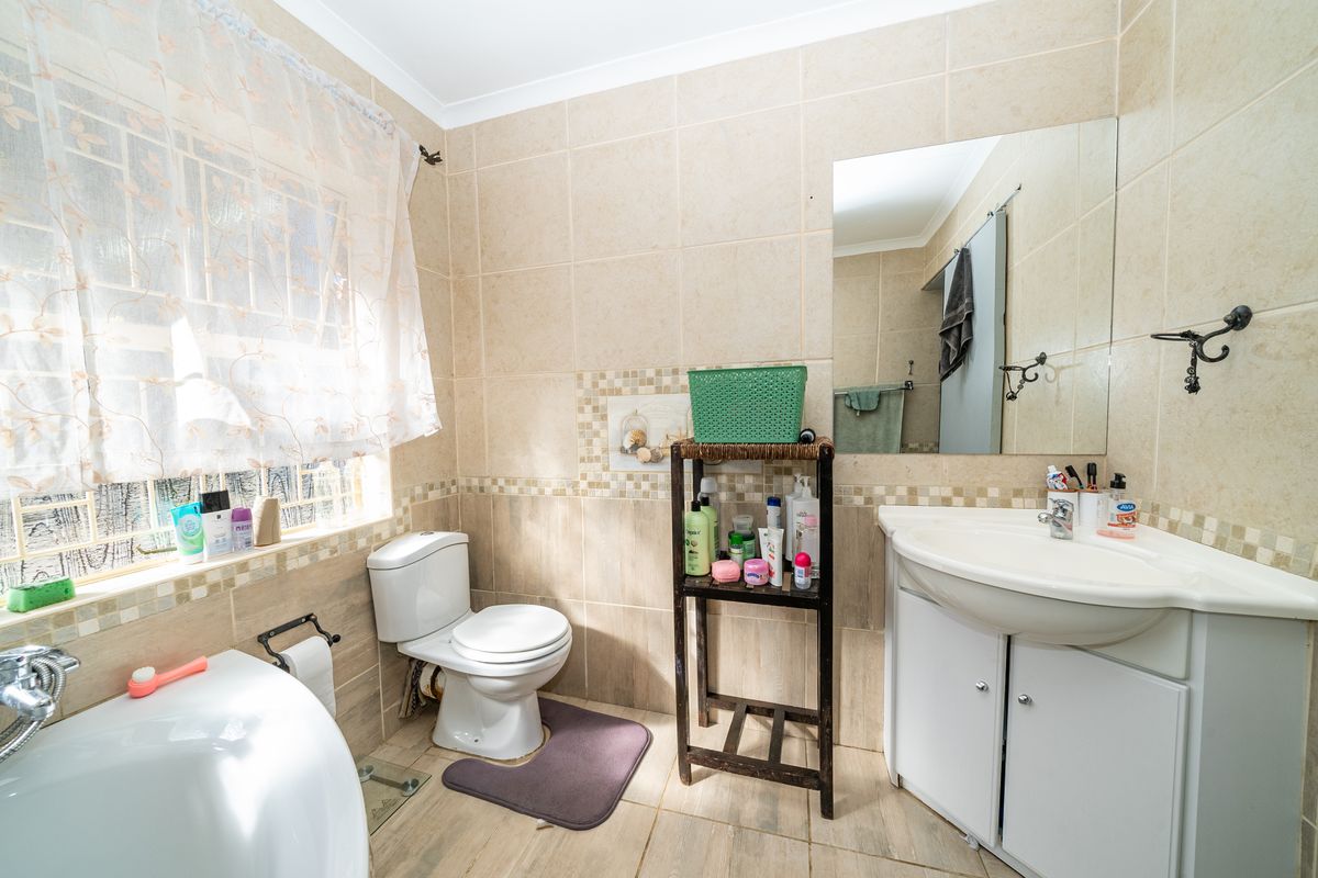 A functional bathroom featuring floor-to-ceiling wall tiles, a vanity basin with storage, a toilet, and a window with security bars.
