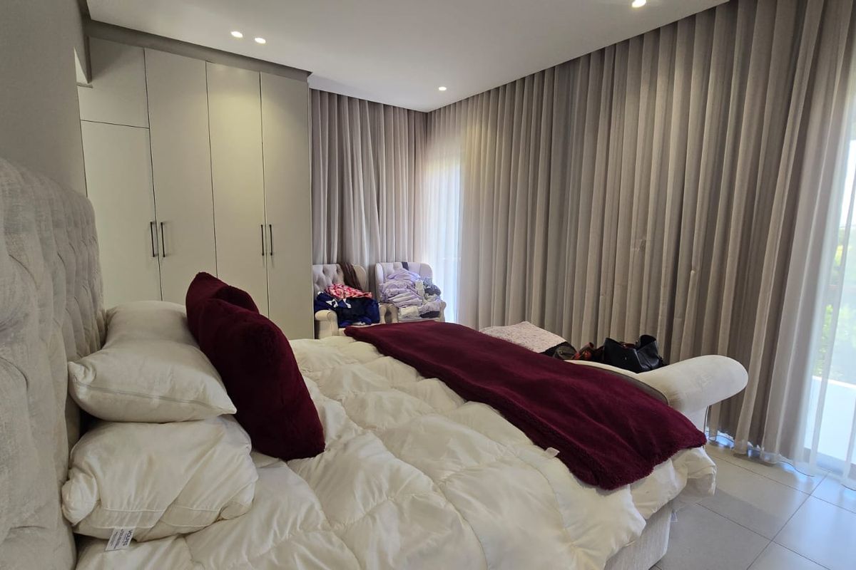 A well-appointed bedroom featuring floor-to-ceiling built-in wardrobes, recessed ceiling lighting, and expansive floor-to-ceiling curtains leading to an outdoor balcony area.