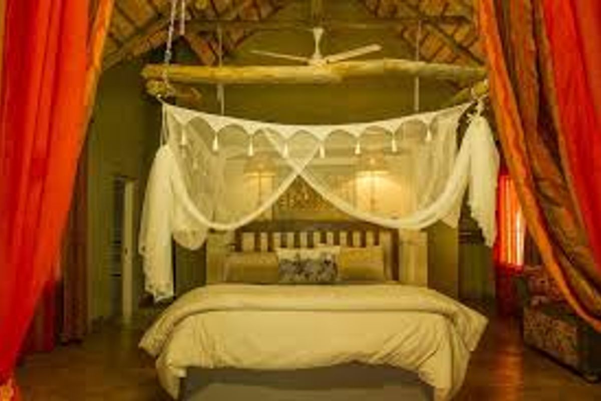 A rustic bedroom featuring a high thatched roof, exposed timber beams, and a ceiling fan, creating a warm and traditional farm-style atmosphere.
